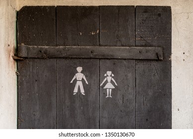 A Door From An Old Outhouse Standing Outside With A Symbol Of A Man And A Woman.
