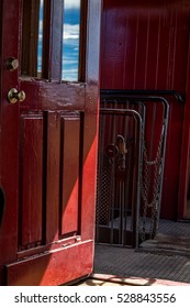 A Door Stands Ajar On A Narrow Gauge Passenger Railroad Car Reflecting The Blue Cloud Streaked Sky In The Window