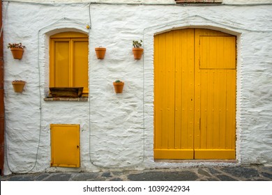 a door and two yellow windows with earthen pots hanging on the white facade