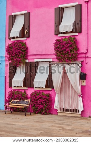 Door and window with flower on the red facade of the house. Colorful architecture in Burano island, Venice, Italy.