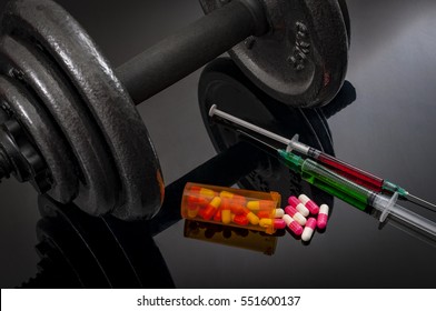 Doping In Sport And Steroid Abuse Concept With A Dumbbell, A Bottle Of Prescription Pills And Syringes With Green And Red Liquid On A Dark Background