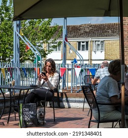 Dorking, Surrey Hills, London UK, August 18 2022, Young Woman Sitting Alone In A Coffee Shop Outside Terrace With Pet Dog Using Mobile Phone