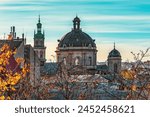 Dormition Church tower and Dominican Church dome in Lviv, Ukraine. Close-up of city roofs against the backdrop of bare tree branches on an autumn morning