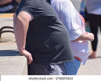 Dorset, UK. May 25 2020. An obese couple standing against a wall in the street. Research shows evidence that obesity and obesity-related conditions seem to worsen the effect of Coronavirus COVID-19. 