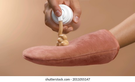 Dosing bronzing lotion or tanning cream from a flask with a doser to a pink tan applicator glove. High quality close-up studio photo image beige background.