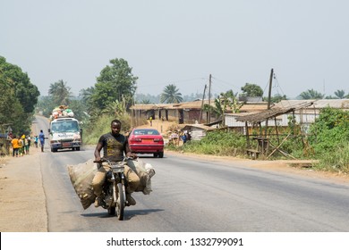 DOUALA, CAMEROON, AFRICA – FEBRUARY 5, 2018: A moped loaded with a sack of corn, in the background a heavily loaded bus, on the way to Douala, Cameroon, Africa.
