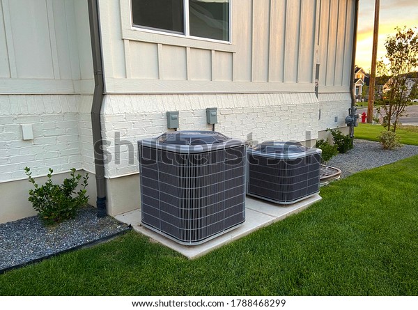 Double AC units outside white brick home with\
green landscape and\
gravel