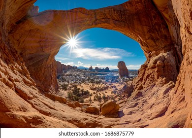 Double Arch in Moab with snow and a sun star in a blue sky