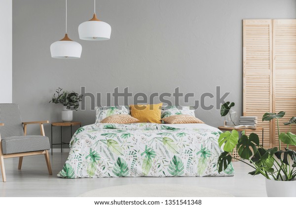 Double bed with botanical accents on sheets and\
peach colored pillows in grey scandinavian bedroom, copy space on\
the empty grey wall