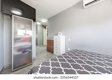 double bed with gray bedspread and matching pillows and plain gray walls, mismatched dressers and air conditioning unit