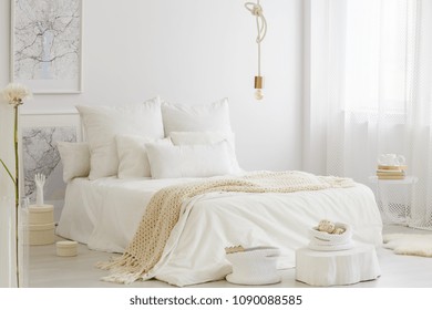 Double bed with knit blanket and white bedding standing in Scandinavian room interior with decor and bulb lamp