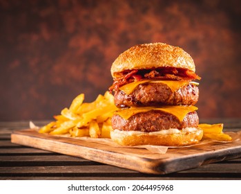 Double beef and bacon burger with cheddar cheese and chips on a wooden board on a table, ready to eat. Size XL. - Powered by Shutterstock