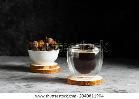 Double bottom glass cup with coffee on a wooden stand with a plate of acorns in a low key