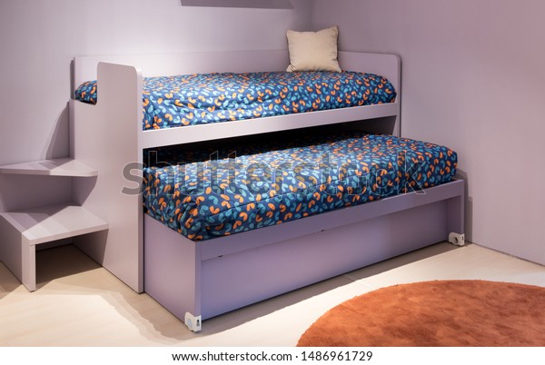 Double bunk bed in a kids bedroom with\
purple decor and colorful bedding offering a solution to two\
children sharing sleeping\
accommodation