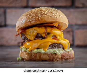 Double Cheese Burger Sandwich With Some Melted Cheddar Cheese, Onion, Lettuce  Placed Isolated On The Center Of A Wooden Surface And Brick Texture Background.