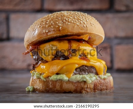 double cheese burger sandwich with some melted cheddar cheese, onion, lettuce  placed isolated on the center of a wooden surface and brick texture background.