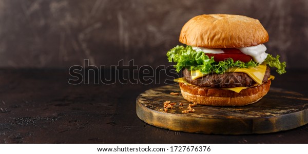 Double cheeseburger with lettuce,\
tomato and melted cheese on wooden board. Long wide\
banner