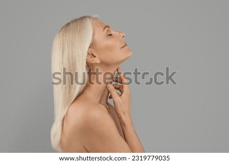 Double Chin Treatment. Beautiful Mature Woman Touching Soft Smooth Skin On Neck, Attractive Elderly Lady With Bare Shoulders Standing Over Light Grey Background, Enjoying Her Beauty, Copy Space