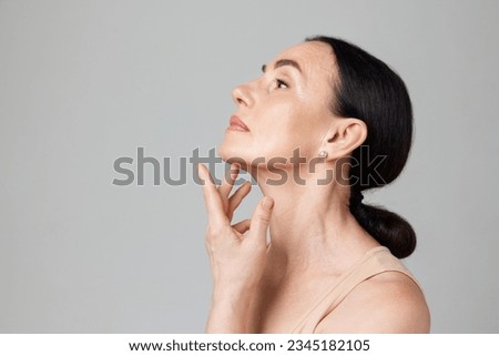 Double chin treatment. Beautiful mature woman touching skin on neck over light grey background. Copy space for ad. Concept of fashion, beauty, spa, cosmetology, skin care, procedures.