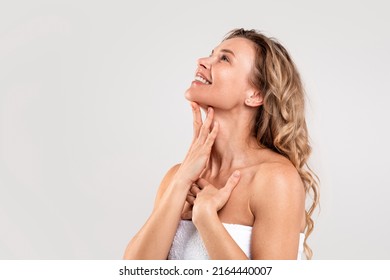 Double Chin Treatment. Beautiful Middle Aged Woman Touching Soft Smooth Skin On Neck, Attractive Mature Lady Standing Wrapped In Towel Over Light Grey Background, Enjoying Her Beauty, Copy Space - Shutterstock ID 2164440007