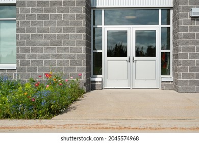 Double Commercial Exterior Doors Of A Business. The Glass Is On Top, Trim Is Stainless Steel Metal. The Doors Have Metal Handles. There Are Large Grey Brick Walls On Both Sides Of The Doors. 