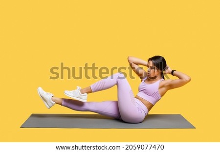 Double crunch excercise. Sporty african american lady working out on mat, doing bicycle crunch abs exercises over yellow studio background, free space