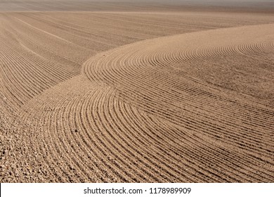 Double Curves Arch Over One Another In Tilled Soil In This Farm Field, A Rough Pattern And Texture For Background.