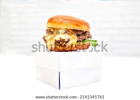 Double decker donut bun burger with beef patties and dressing on a takeaway box.