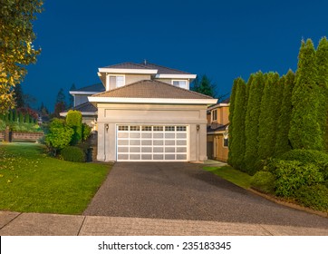 Double Doors Garage With Wide And Long Driveway  To A Big Luxury House At Night, Dusk Time In Suburbs Of Vancouver, Canada.