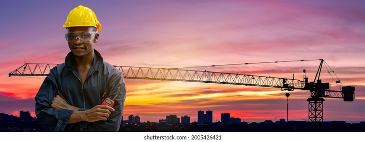 Double exposure african architect wearing uniform holding radio comunication under work and inspection with tower crane consturction building twilight sky background.
