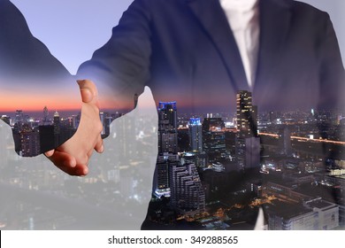 Double exposure of business handshake and night city as commitment, economy, partnership and investment concept.