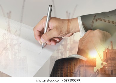 Double exposure of businessman hand holding a pen signing to the document, construction crane, building and sunlight of sunset as business approval and industrial concept.