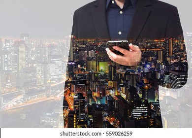 Double exposure - businessman using smartphone with city overlay