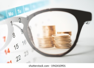 Double Exposure Of Calendar And Stack Of Coins Behind Blurred Glasses For Business And Finance Background