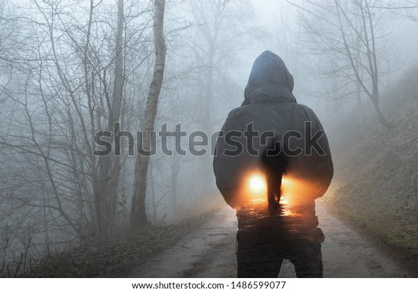 A double exposure concept. A\
hooded figure looking at a silhouette of a man in front of car\
headlights. On a spooky forest track on a misty winters\
evening.