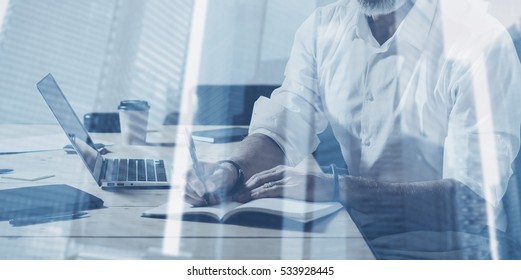 Double exposure concept.Adult bearded businessman working with laptop at the wood table in modern coworking place.Skyscraper building on the blurred background.Wide,film effect - Shutterstock ID 533928445