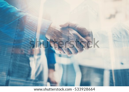 Double exposure concept.Close up view of business partnership handshake concept.Photo two businessman handshaking process.Skyscraper office building on the blurred background.Horizontal,flares effect