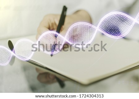 Double exposure of creative DNA hologram and man hand writing in notebook on background. Bio Engineering and DNA Research concept