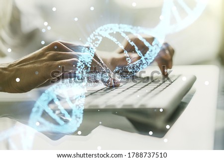 Double exposure of creative DNA hologram and hands typing on laptop on background. Bio Engineering and DNA Research concept