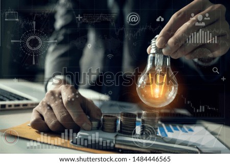 Double exposure of graph and rows of coins for finance and business concept. business man hand holding lightbulb with using calculator to calculate and money stack. Out of focus. 
