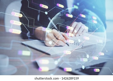 Double exposure of hands making notes with world map hologram and data theme icons. Concept of global computer data.