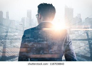 The Double Exposure Image Of The Business Man Standing Back During Sunrise Overlay With Cityscape Image. The Concept Of Modern Life, Business, City Life And Internet Of Things.