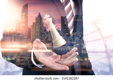 The double exposure image of the businessman hold a chess king on hand overlay with cityscape image. the concept of strategic, planning, management, intelligence and education.