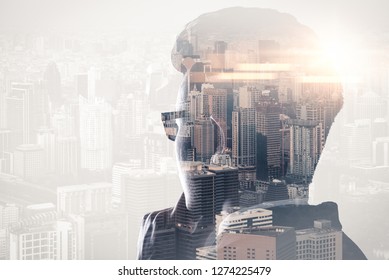 The double exposure image of the businessman standing back during sunrise overlay with cityscape image. The concept of modern life, business, city life and internet of things.