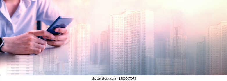 Double Exposure Of A Man's Hand Holding A Cellphone And Building In Cityscape, Technology In Modern City Life, Commercial, Trade And Property Investment Concept In Panoramic For Banner.