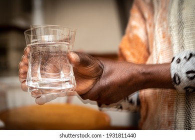 Double exposure that creates a blurry effect on the foreground of an African lady's hands as she tries to steadily hold a glass. Concept of difficulties due to the tremors of Parkinson's disease