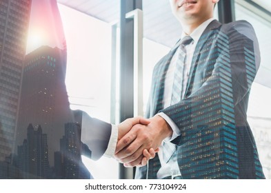 Double exposure of two businessmen reaching an agreement and making handshake with abstract construction building - Greeting and dealing real estate business concepts.