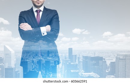 Double exposure of an unrecognizable crossed arms businessman standing against a city panorama. Mock up