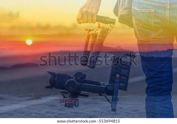 Double exposure Videographer with\
gimball video DSLR with Sunrise in the morning background\
