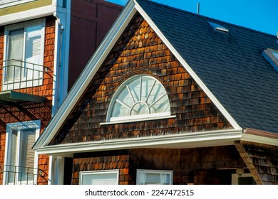 Double gable style roof with gray tiles and aged and weathered exterior facade made of wood with white accent paint. In a row of modern houses as detail in the historic districts of san francisco.